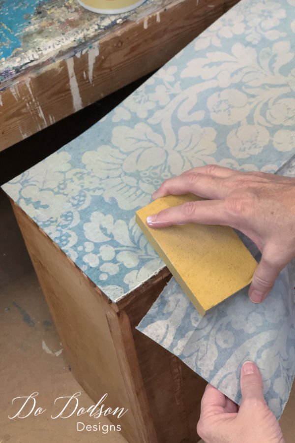 While the top coat is still wet, use a fine grit sanding block to carefully trim the extra decoupage paper away. 
