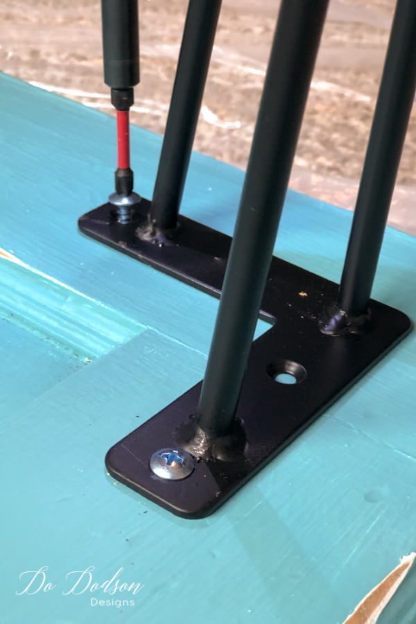 Secure the hairpin legs with screws. Be sure and pre-drill the holes to prevent cracking and splitting of the wood door.