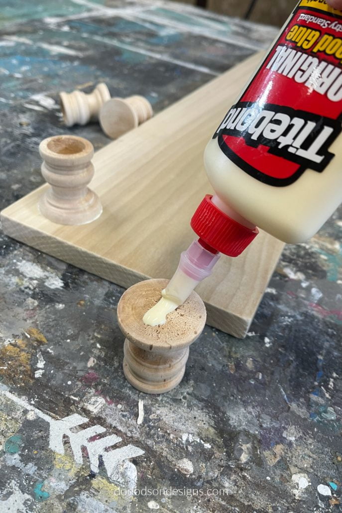 Add wood glue to the bottom side of the wood candle cups and attach them to all four corners of the board and allow them to dry. These will be the feet of the table riser. 