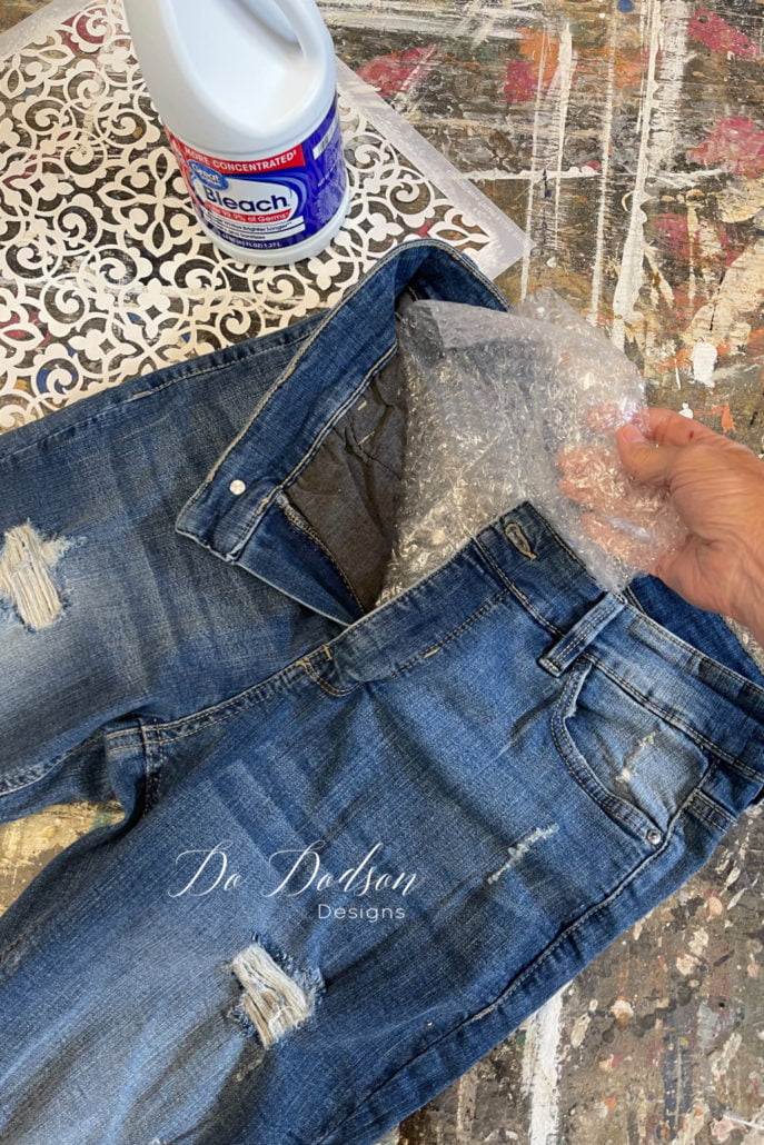 Next, you'll need to place something inside the jean leg to prevent the bleach from soaking through before you spray bleach over the stencil.