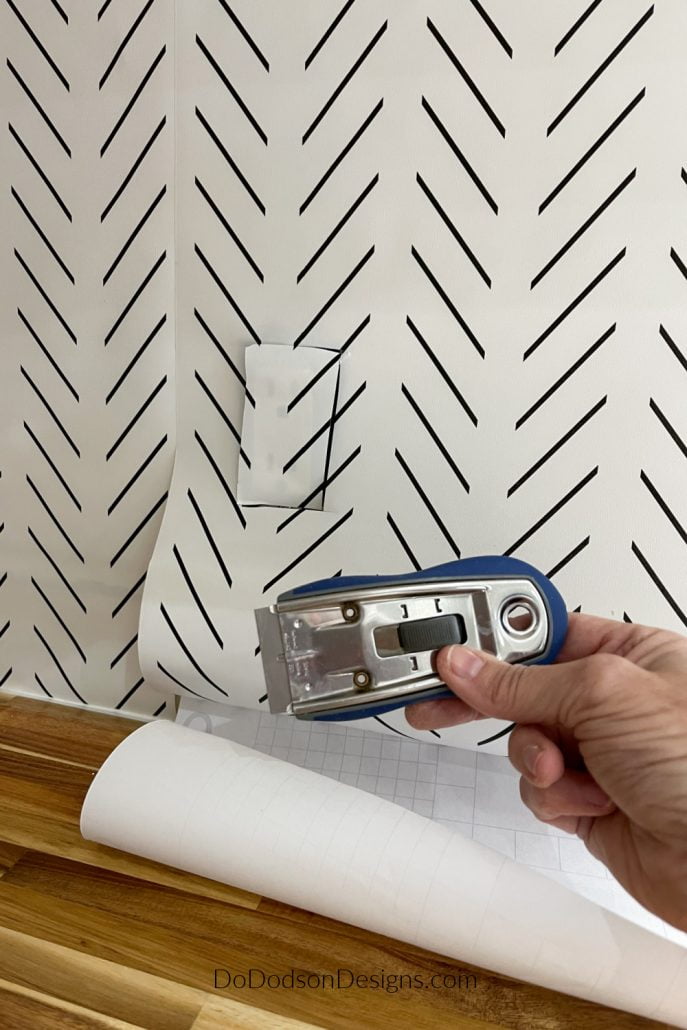 Once you have the DIY peel and stick wallpaper backsplash in place, use a utility knife to carefully remove the excess at the bottom of the paper and cut around electrical outlets. 